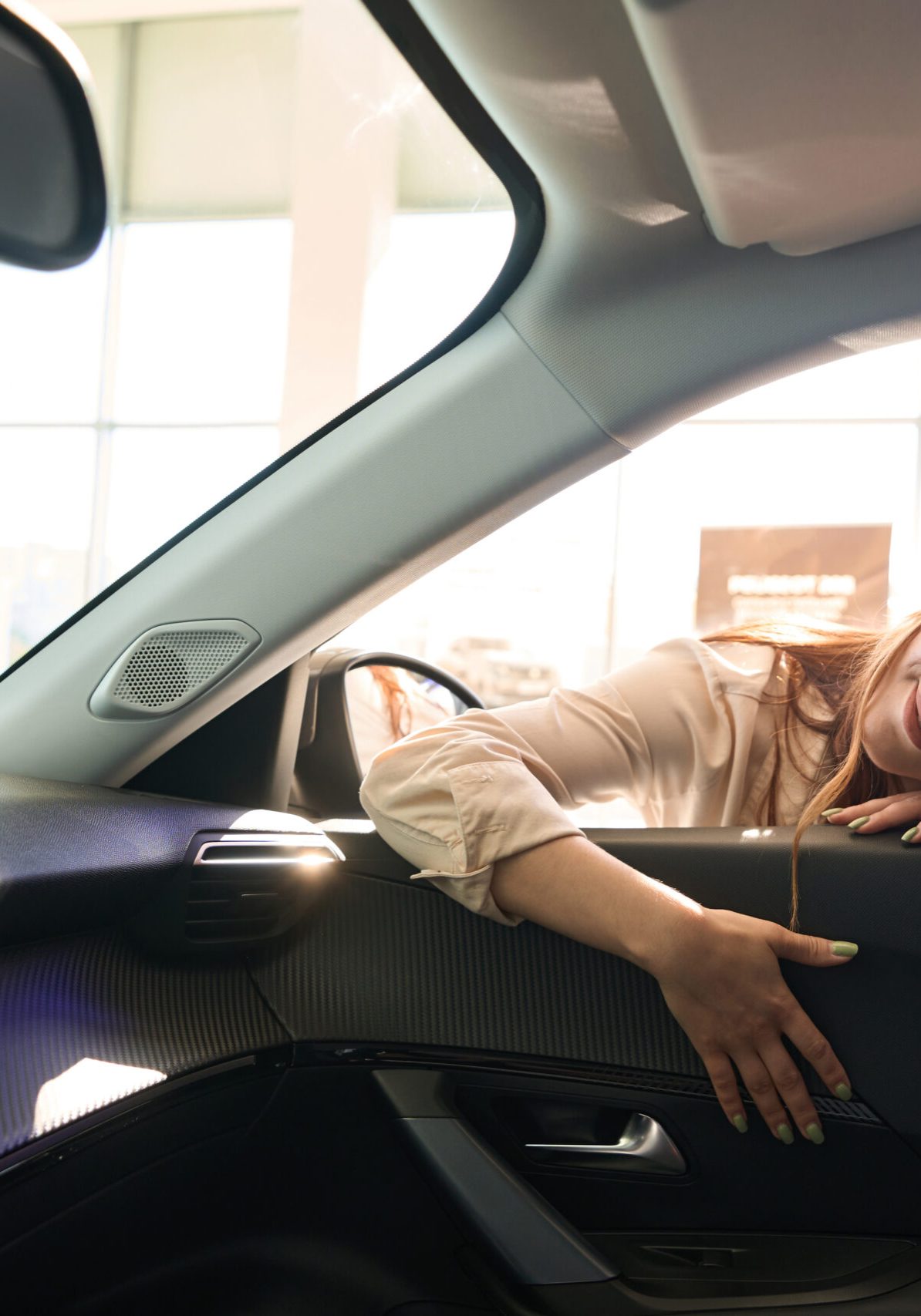 Smiling young woman lying on lower car window edge and touching automotive upholstery quality